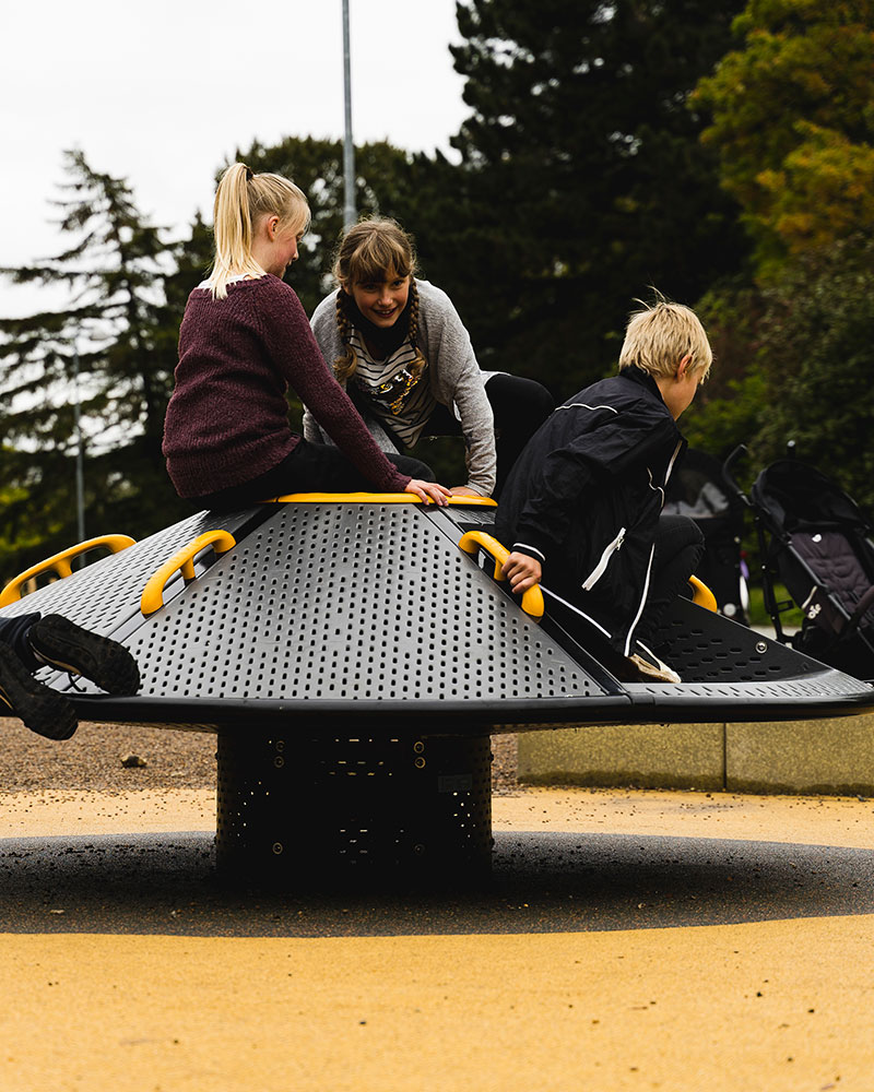 Een groep kinderen klimt op, zit en houdt zich vast aan de spijlen van een grote rotonde.